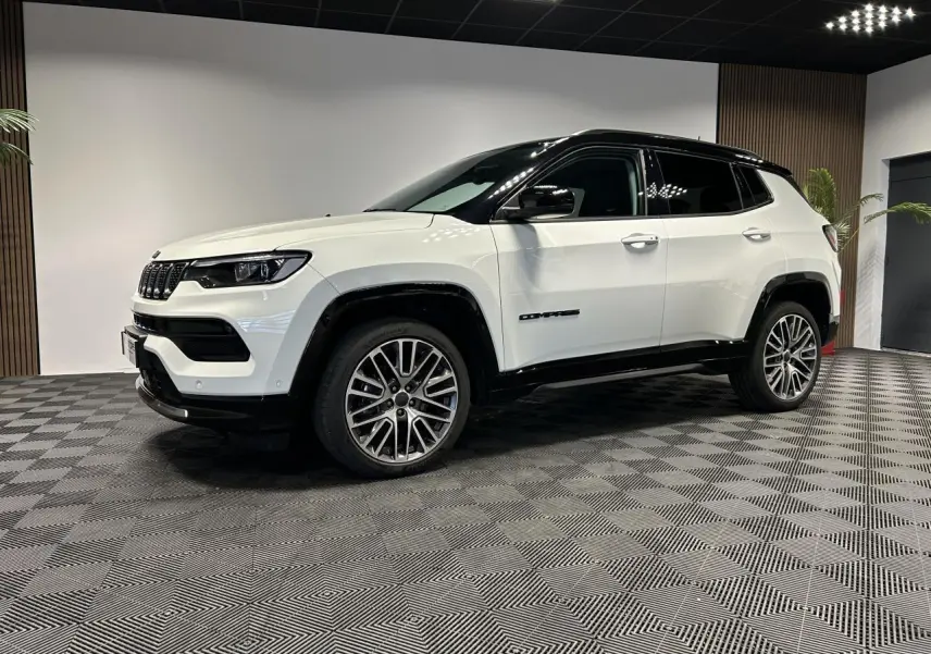 Jeep Compass blanc vue 3/4 avant droit avec toit noir et jantes alliage 19 pouces dans un showroom.