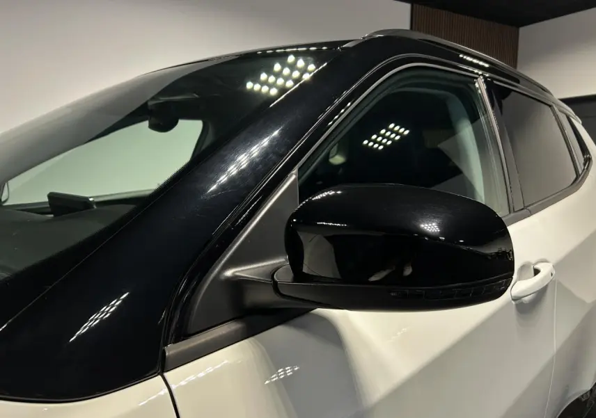 Gros plan sur le rétroviseur côté gauche noir brillant du Jeep Compass blanc avec toit noir, intérieur visible à travers la vitre.