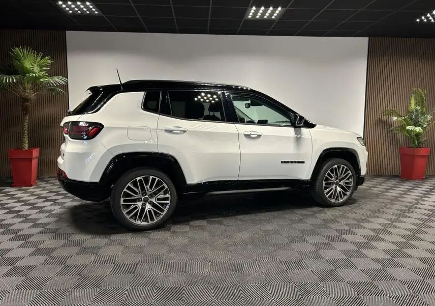 Jeep Compass blanc avec toit noir vu de profil côté gauche, jantes alliage 19 pouces et barres de toit noires.