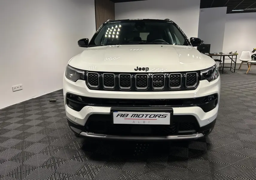 Vue frontale d'un Jeep Compass blanc avec calandre noire et toit noir dans un showroom intérieur.