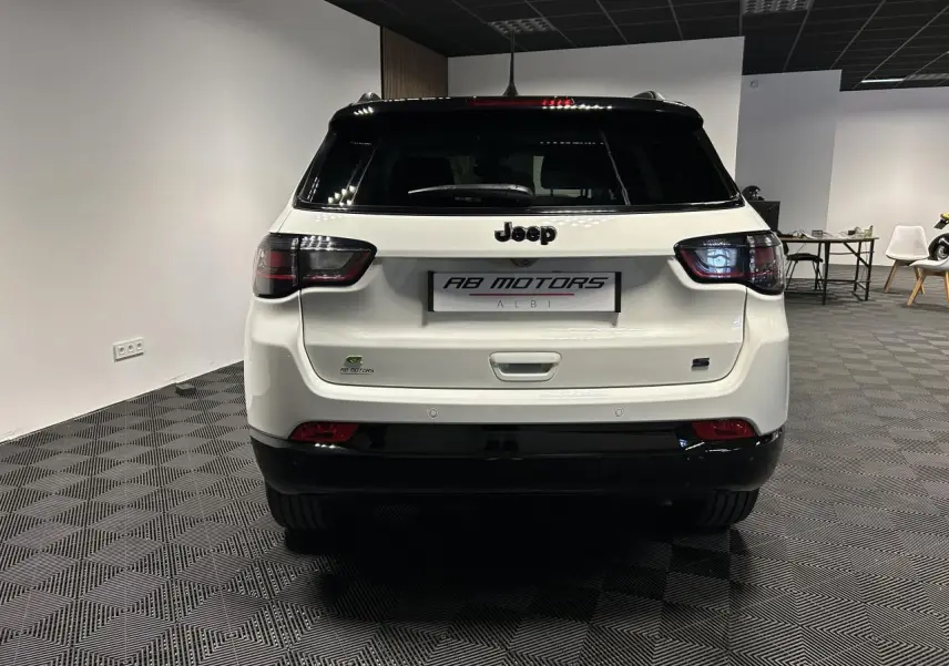 Vue arrière d'un Jeep Compass blanc avec toit noir, feux arrière LED et logo Jeep bien visible.