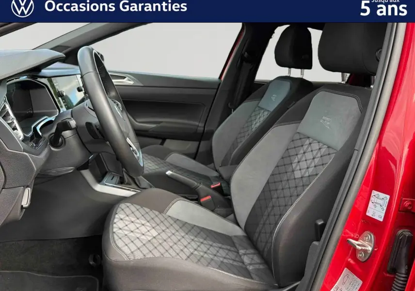 Vue intérieure côté conducteur de la Volkswagen Polo rouge 2025, sièges tissu gris avec surpiqûres et volant cuir.