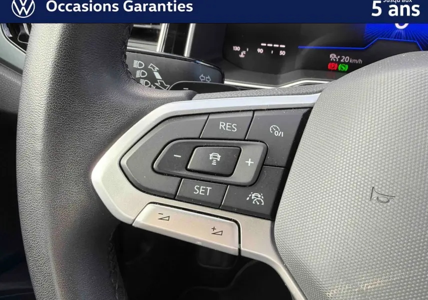 Gros plan sur les commandes au volant côté gauche du Volkswagen Polo rouge, avec affichage digital en arrière-plan.