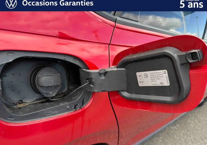 Gros plan sur la trappe à carburant ouverte côté gauche d'une Volkswagen Polo rouge métallisée.