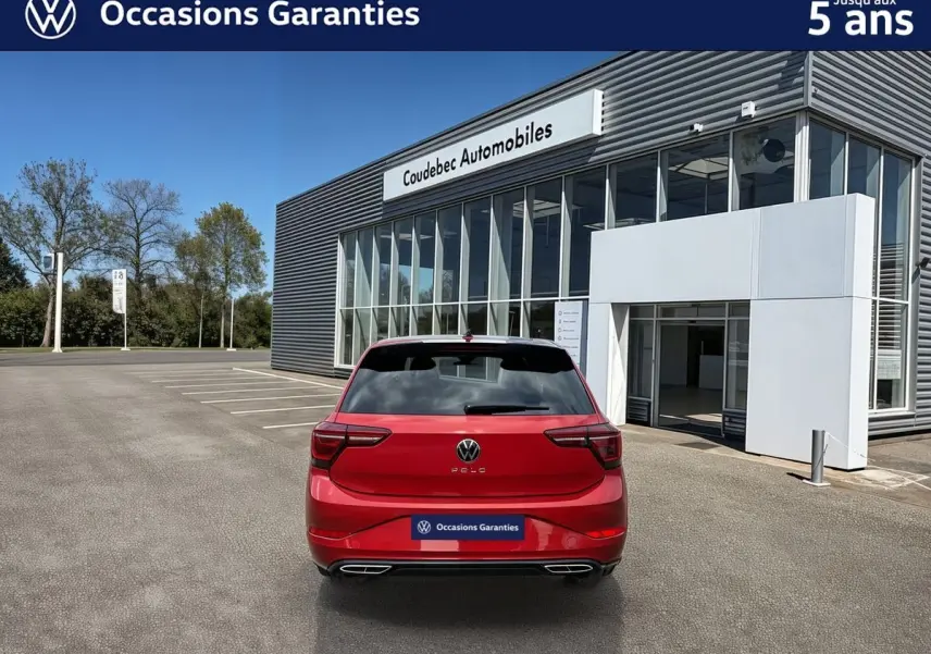 Vue arrière d'une Volkswagen Polo rouge métallisée stationnée devant un bâtiment moderne de concession automobile.