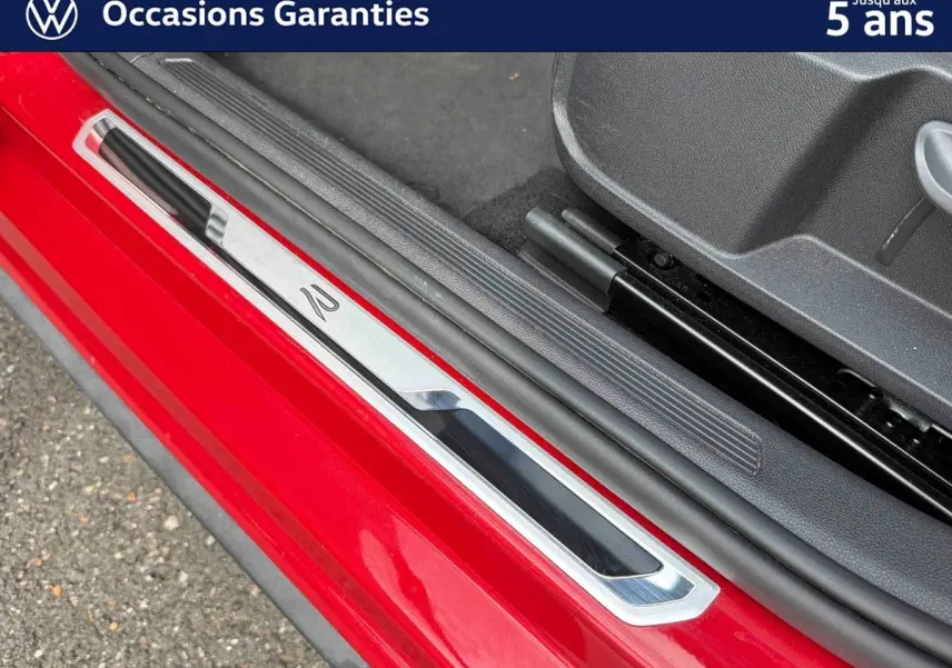 Gros plan sur la seuil de porte côté conducteur rouge métallisé de la Volkswagen Polo 2025 avec insert chromé et logo R.