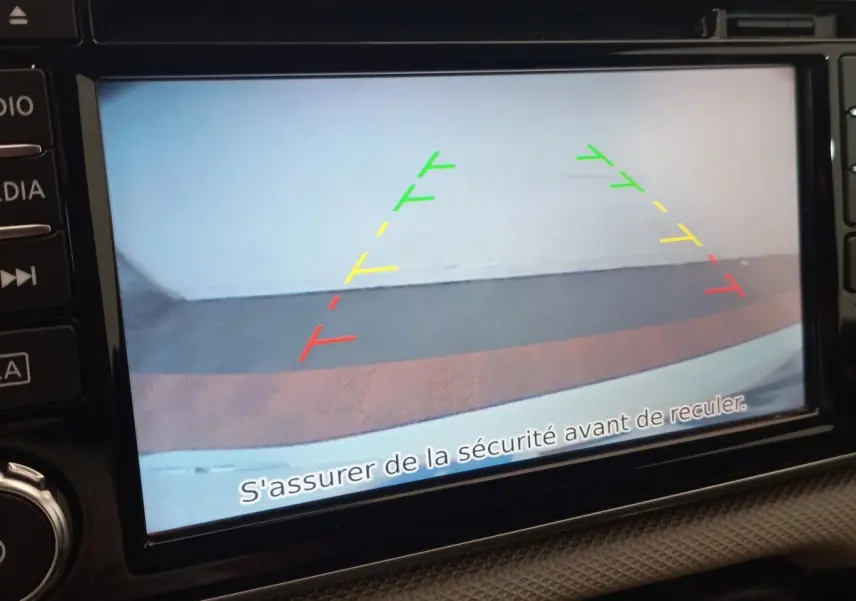 Écran tactile de la Nissan Micra blanc montrant la caméra de recul avec guidage coloré et message de sécurité.