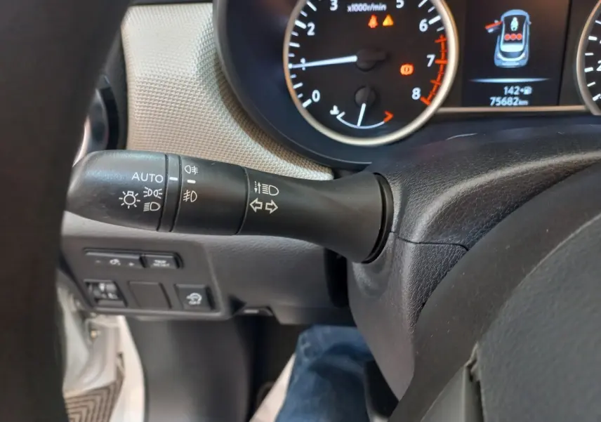 Gros plan sur le commodo gauche du volant noir d'une Nissan Micra blanche, avec tableau de bord et compte-tours en arrière-plan.
