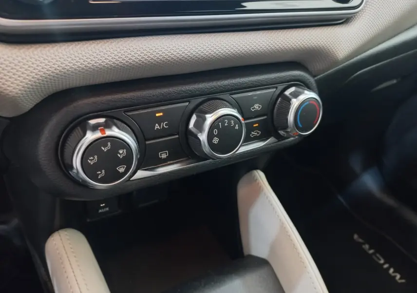 Gros plan sur les commandes de climatisation noires et argentées du tableau de bord d’une Nissan Micra blanche.