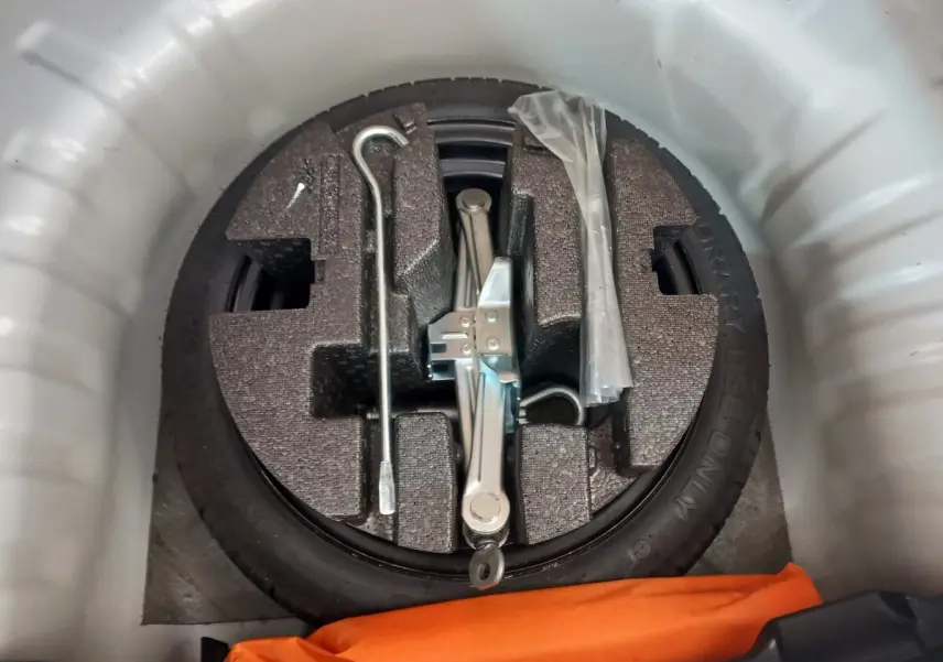 Roue de secours galette noire avec cric et outils dans le coffre blanc d’une Nissan Micra IG-T 90 Business Edition.