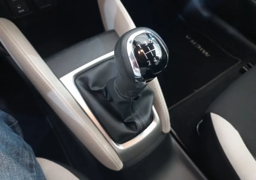 Gros plan sur le levier de vitesse manuel noir entouré de garnitures beiges dans l’habitacle d’une Nissan Micra blanche.
