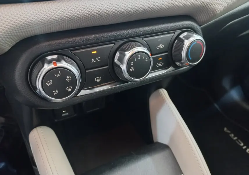 Gros plan sur les commandes de climatisation noires et argentées dans l'habitacle d'une Nissan Micra blanche.