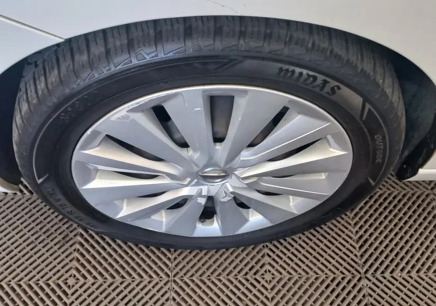 Gros plan sur la roue avant droite d’une Nissan Micra blanche, jante en alliage avec logo Nissan au centre.