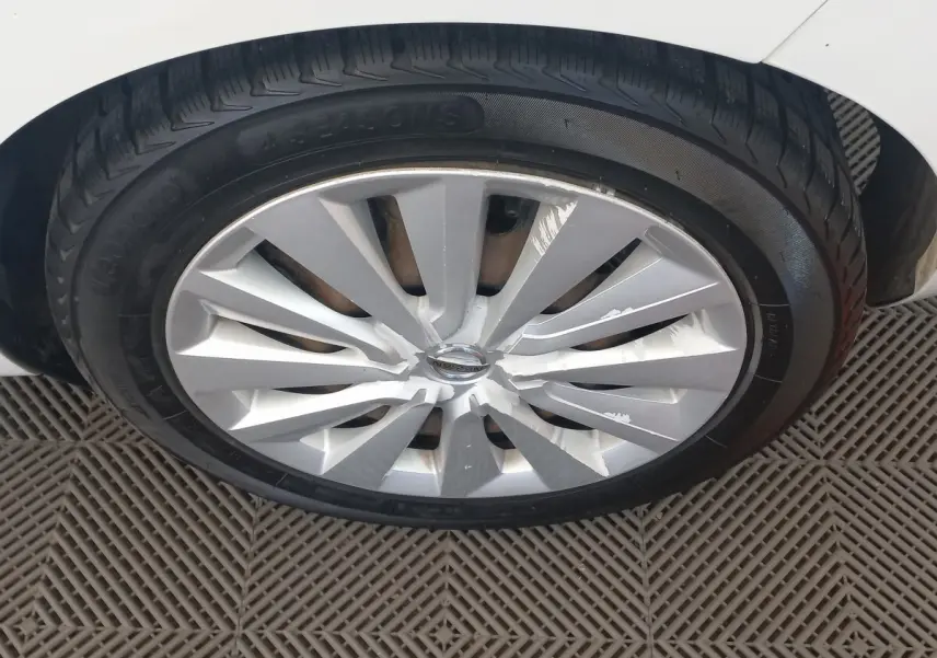 Gros plan sur la roue avant gauche d'une Nissan Micra blanche, jante en alliage avec éclats de peinture visibles.