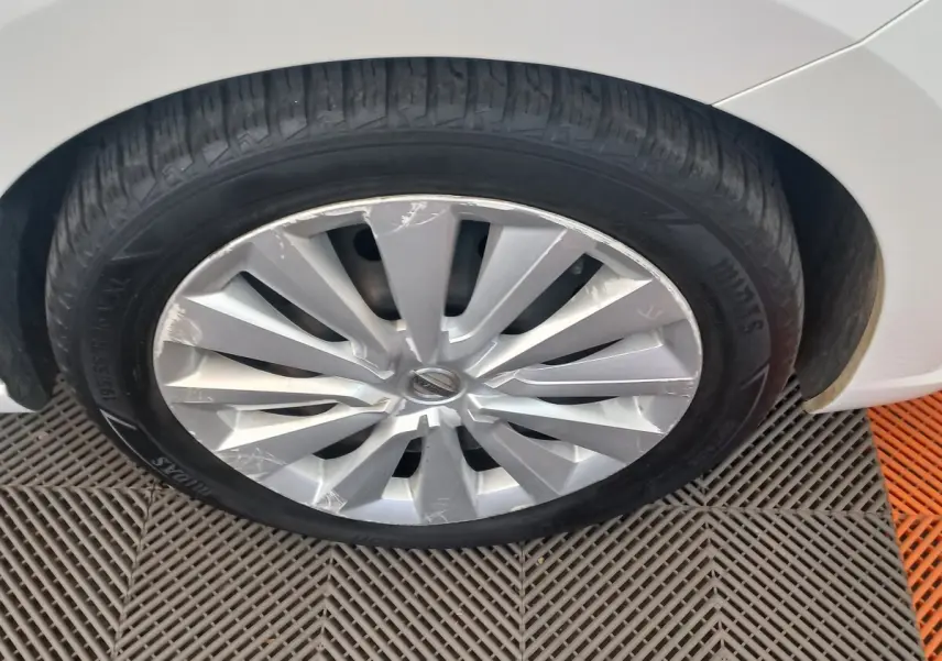 Gros plan sur la roue avant droite d'une Nissan Micra blanche, jante en alliage avec rayons en V marqués.