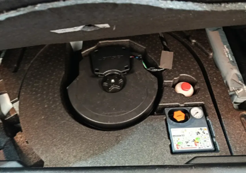 Vue rapprochée du coffre du Renault Kadjar blanc, montrant le logement de la roue de secours et les accessoires de gonflage.