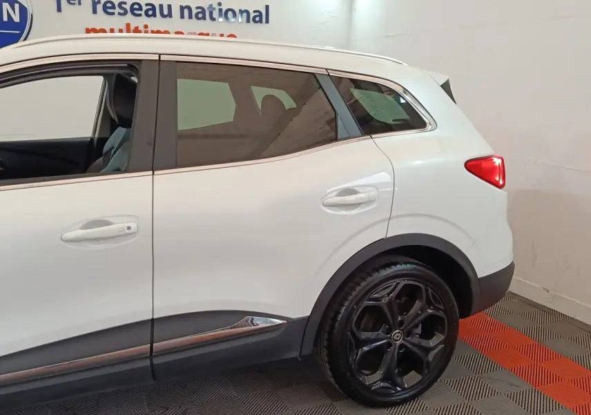 Vue de profil côté droit sur la partie arrière d'un Renault Kadjar blanc avec jantes noires et feux arrière allumés.