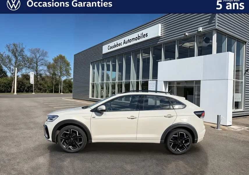 Profil côté gauche du Volkswagen Taigo gris clair garé devant un bâtiment moderne avec grandes baies vitrées.