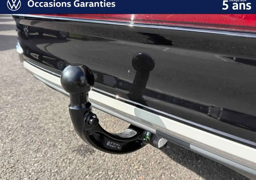 Gros plan sur l'attelage amovible noir fixé à l'arrière d'un Volkswagen Taigo gris, avec pare-chocs et feu arrière visibles.