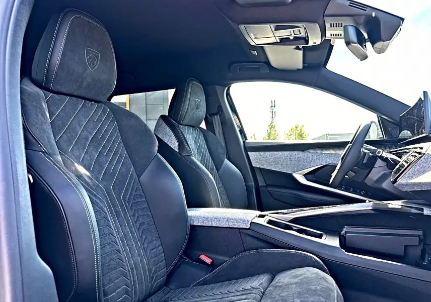 Vue intérieure côté conducteur du Peugeot 5008 Hybrid 145 GT e-dcs6 2025, sièges noirs en cuir et alcantara avec surpiqûres blanches.