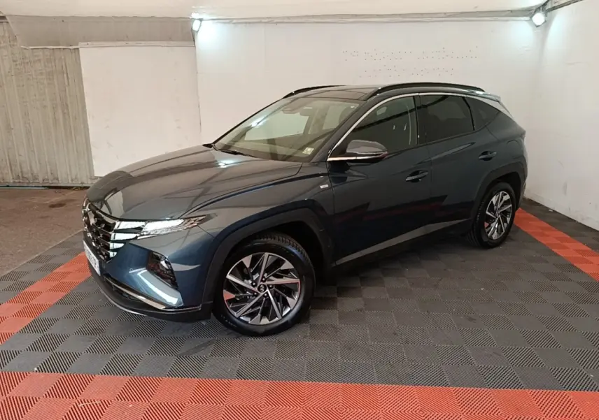 Vue 3/4 avant droit du Hyundai Tucson bleu métallisé avec jantes alliage et toit noir dans un garage.