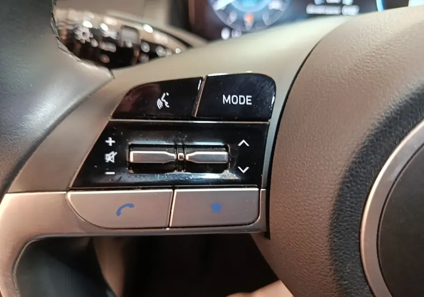 Gros plan sur les commandes gauche du volant gris du Hyundai Tucson bleu 2021, avec boutons mode et téléphone.