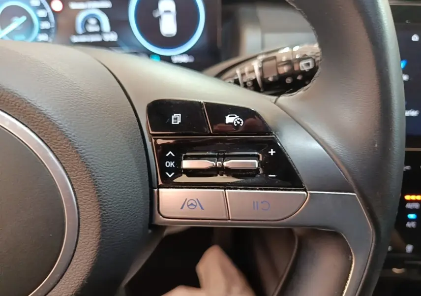Gros plan sur les commandes du volant cuir et alu du Hyundai Tucson bleu 2021, avec affichage digital en arrière-plan.