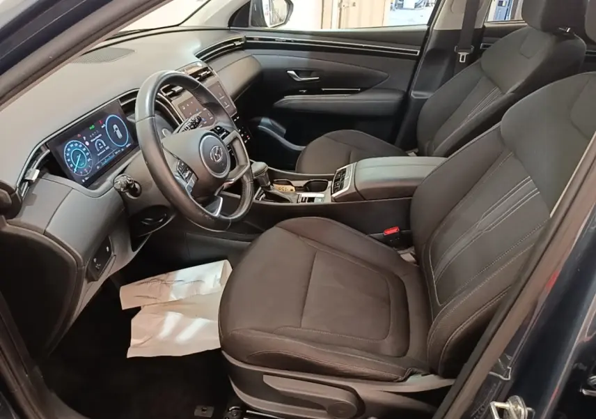 Intérieur du Hyundai Tucson 2021 vu côté conducteur, sièges noirs et tableau de bord avec écran digital.
