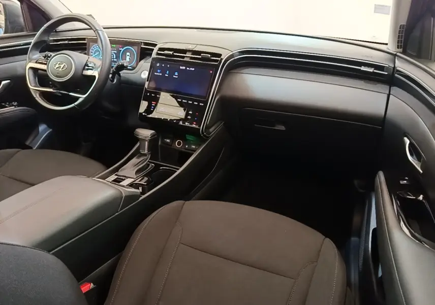 Vue intérieure avant droite du Hyundai Tucson 2021, tableau de bord noir avec écran tactile central et volant multifonctions.