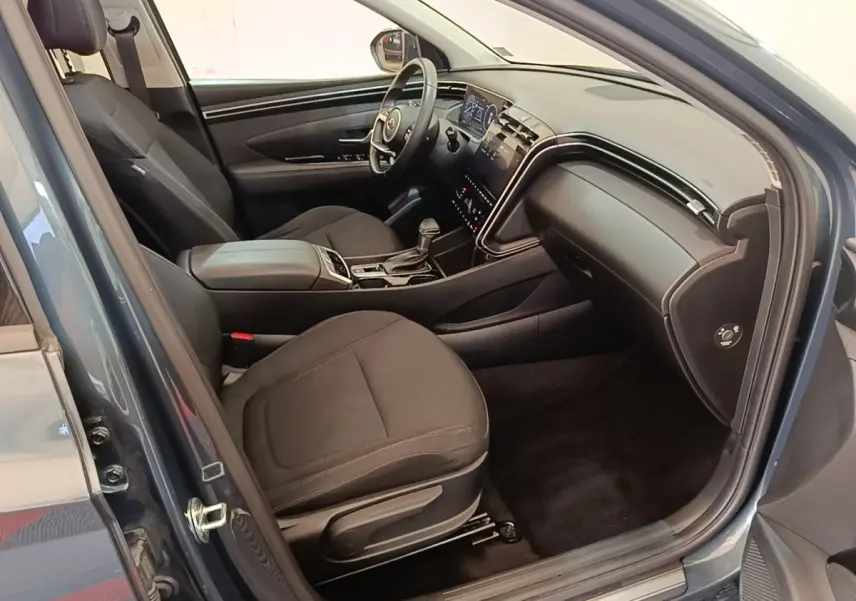 Vue intérieure côté conducteur du Hyundai Tucson bleu 2021, montrant sièges noirs et tableau de bord digital.