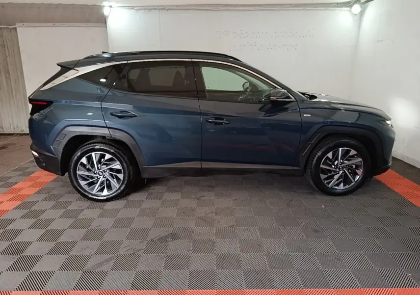 Vue de profil côté gauche d’un Hyundai Tucson bleu 2021 avec jantes alliage et toit noir dans un garage.
