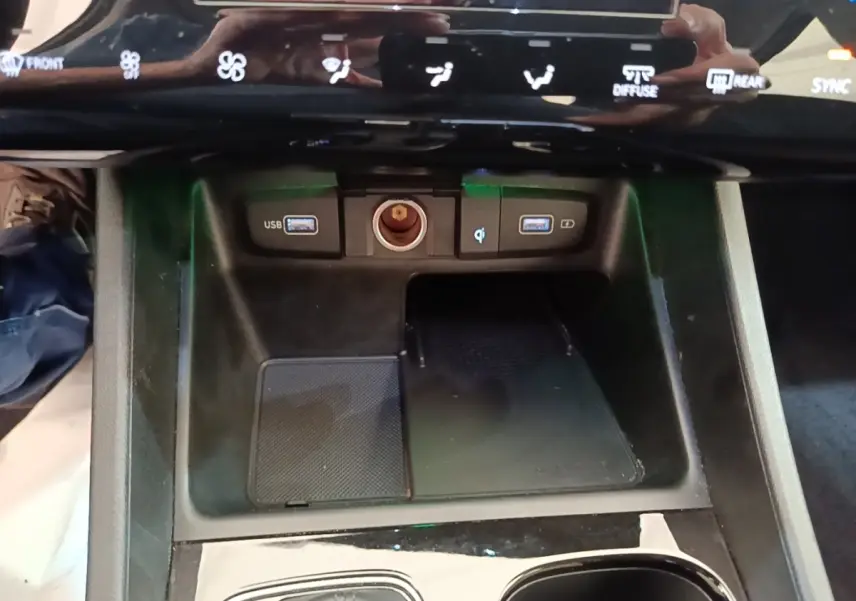 Gros plan sur la console centrale noire du Hyundai Tucson hybride 2021 avec ports USB, prise 12V et zone de recharge sans fil.
