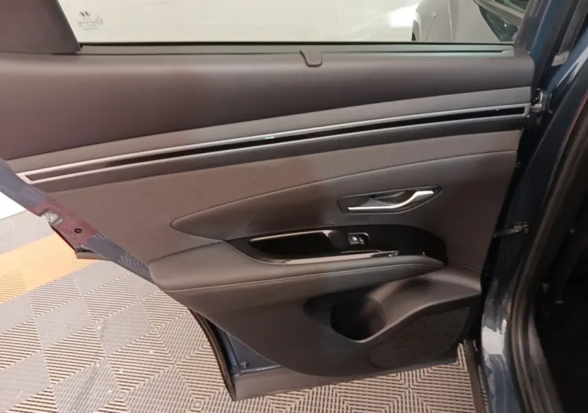 Vue intérieure de la porte arrière droite du Hyundai Tucson bleu, avec garniture noire et commandes de fenêtre.
