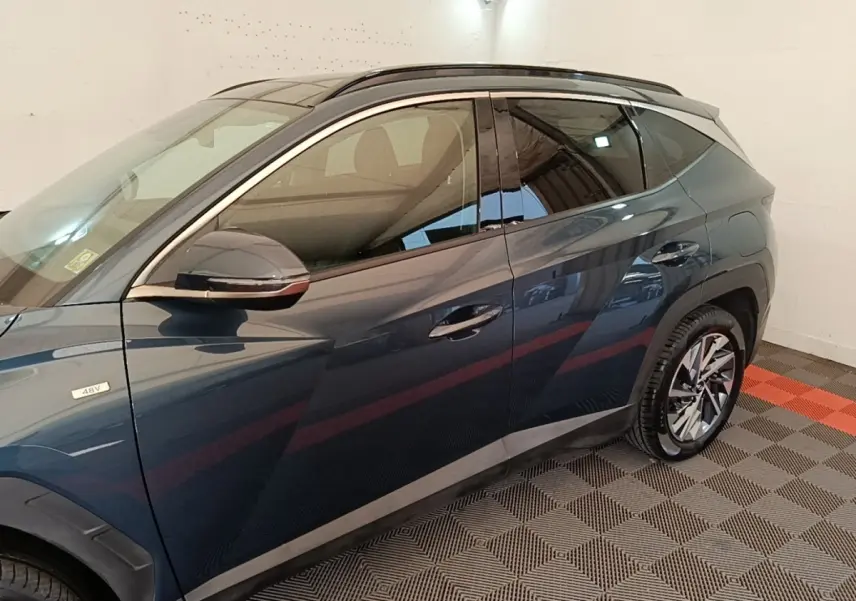 Vue côté gauche du Hyundai Tucson bleu hybride 48V, mettant en valeur les jantes alliage et le rétroviseur chromé.