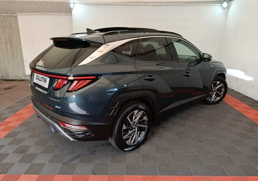 Vue 3/4 arrière droite d’un Hyundai Tucson bleu foncé avec toit noir et feux arrière LED distinctifs dans un garage.