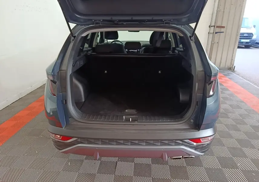 Vue arrière du Hyundai Tucson bleu 2021 avec coffre ouvert montrant un espace de chargement spacieux et intérieur sombre.