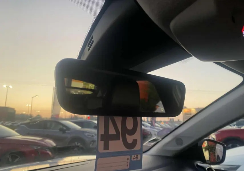 Vue intérieure centrée sur le rétroviseur intérieur d'une Citroën C4 blanche, avec parking en arrière-plan au crépuscule.