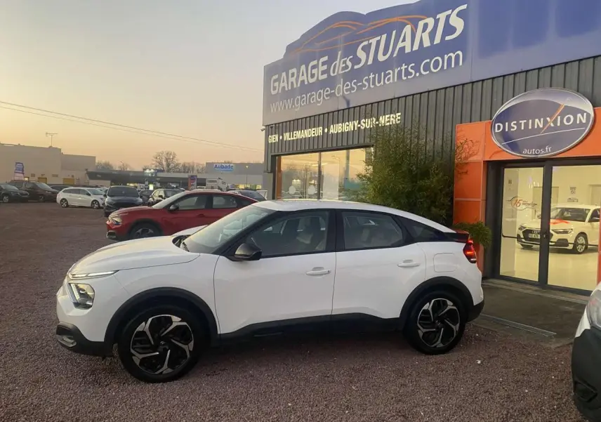 Citroën C4 blanc vue de profil côté gauche, garée devant un garage avec jantes noires et toit noir contrastant.