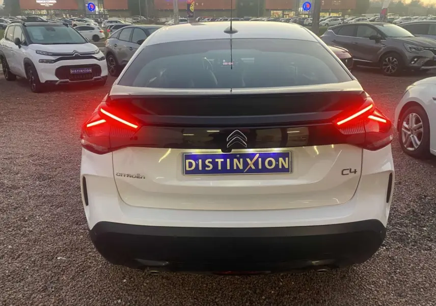 Vue arrière d'une Citroën C4 blanche de 2021 avec feux arrière allumés et plaque Distinxion visible.