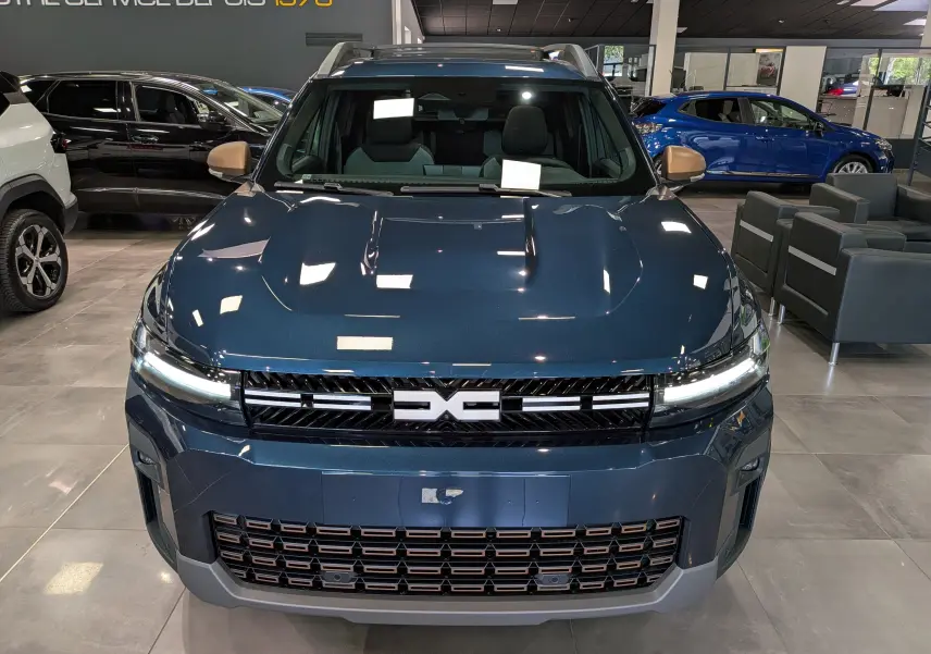 Vue avant d'un Dacia Bigster bleu indigo en showroom, avec calandre noire et détails cuivrés sur le pare-chocs.
