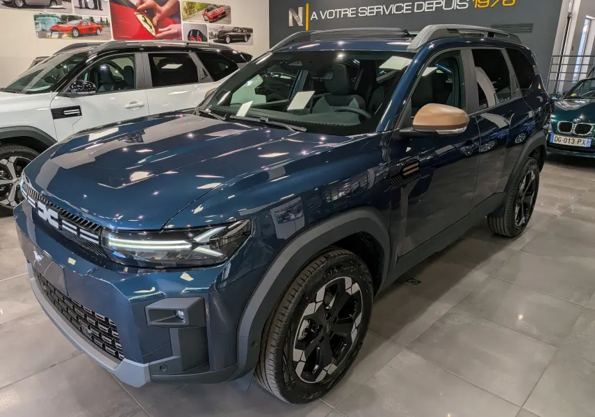 Vue 3/4 avant droit du Dacia Bigster bleu indigo avec rétroviseurs couleur beige et jantes noires en concession.