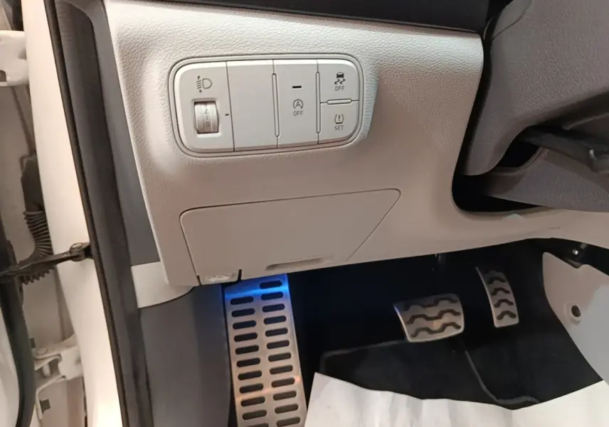 Détail intérieur côté conducteur du Hyundai Bayon blanc 2024, avec commandes d'éclairage et pédales en aluminium.