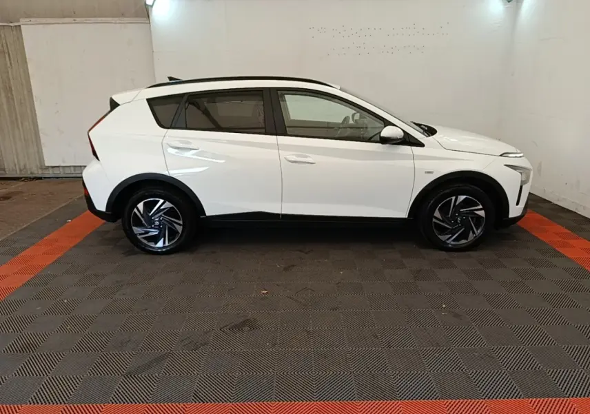 Vue de profil côté droit d'un Hyundai Bayon blanc 2024 avec jantes alliage et toit noir dans un garage.