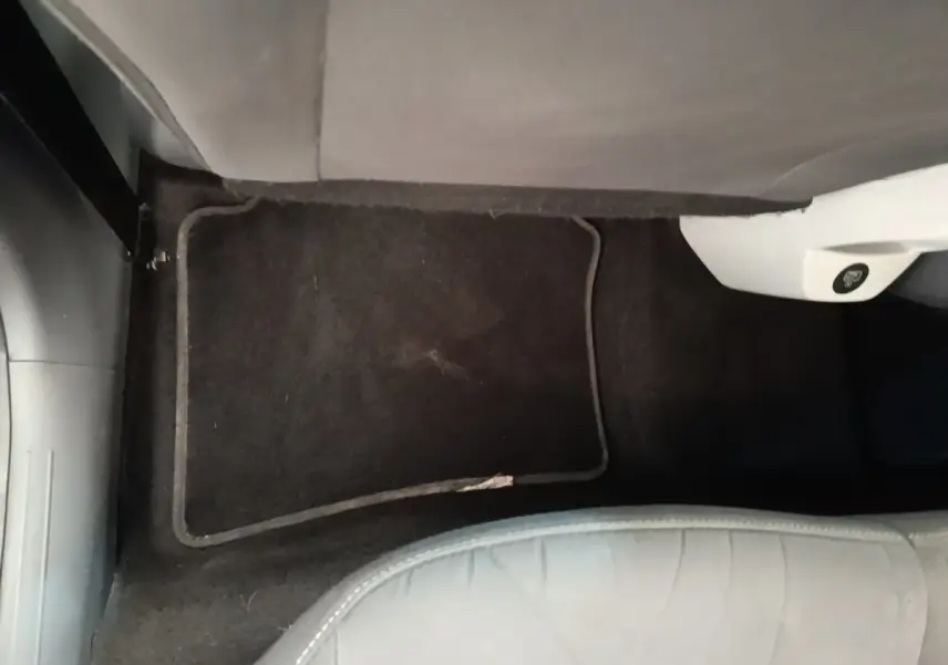 Vue intérieure du sol côté passager avant du Hyundai Bayon 2024 blanc avec tapis de sol noir et partie inférieure de siège visible.