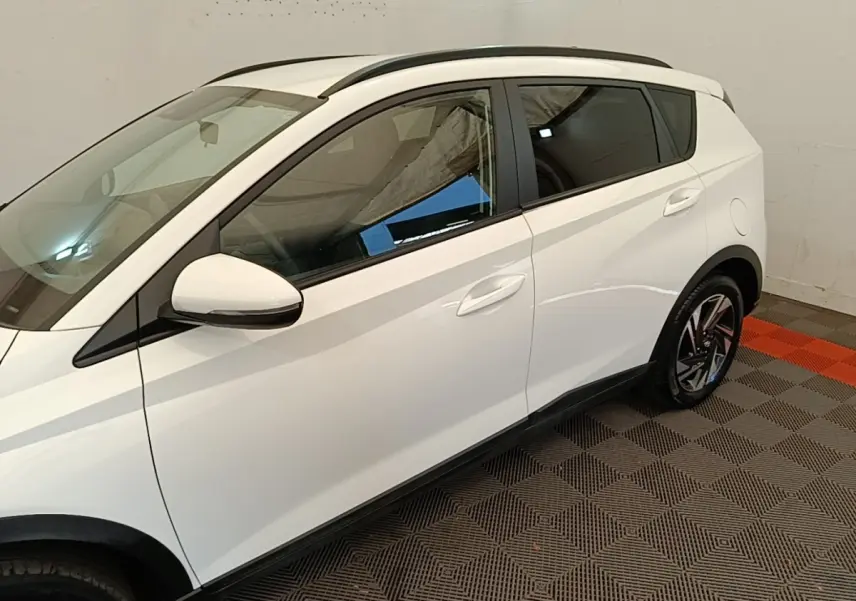 Vue latérale droite d'une Hyundai Bayon blanche 2024 avec jantes alliage et rétroviseurs blancs dans un garage.