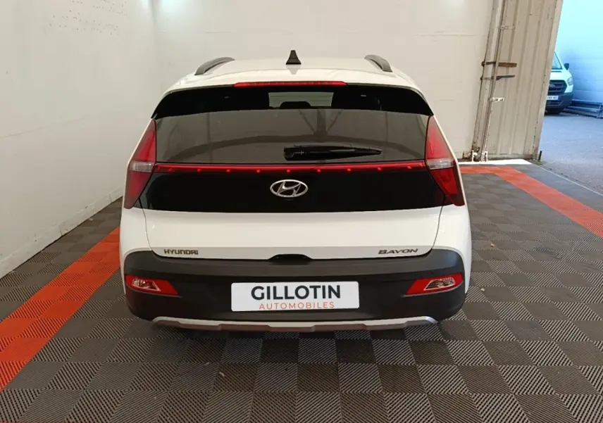 Vue arrière d'une Hyundai Bayon blanche 2024 avec feux arrière reliés par une bande lumineuse rouge.