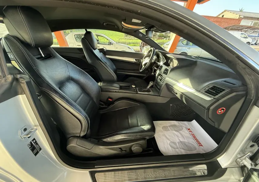 Intérieur noir cuir de la Mercedes Classe E 250 Coupé 2.2 CDI, vue côté gauche avec tableau de bord et sièges avant visibles.