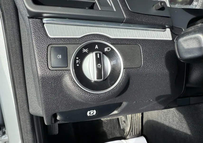 Gros plan sur le bouton de commande des phares et frein à main électrique dans une Mercedes Classe E 250 Coupé gris.