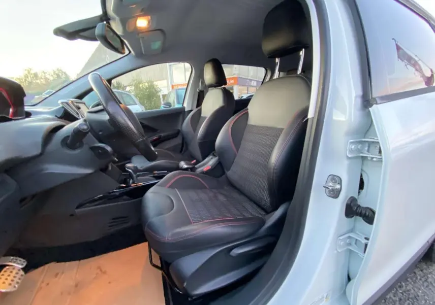 Vue intérieure côté conducteur d'un Peugeot 2008 blanc, sièges noirs avec surpiqûres rouges et volant cuir.