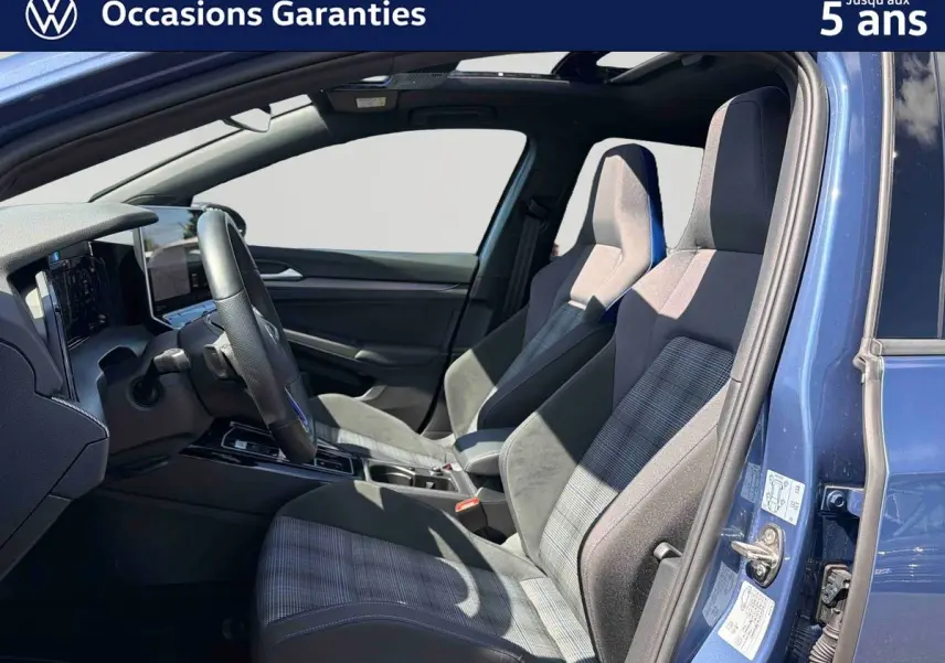 Vue intérieure côté gauche d'une Volkswagen Golf 1.5 eHybrid 2025 bleu, sièges sport haut de gamme avec tissu à motif écossais.